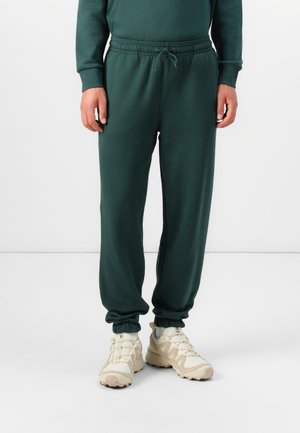 Green cotton joggers with an elastic waistband and ankle cuffs. Smooth texture, minimal design, and functional drawstring detail.