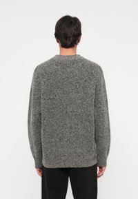 Grå strikket genser med rund hals og lange ermer, med en teksturert finish og ribbede mansjetter ved kanten og halsen.