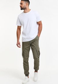 Vit bomullströja i kombination med olivgröna cargobyxor med sidfickor och åtsittande muddar, kompletterad med vita sneakers.