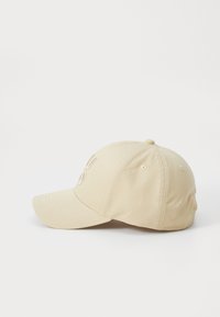Light beige baseball cap made of fabric, featuring a curved brim and embroidered logo on the front. Smooth texture with eyelet vents.