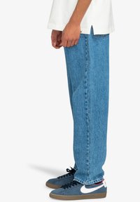 Jeans de mezclilla de color azul claro, de corte recto y holgado; presentan costuras visibles y un diseño clásico de cinco bolsillos.