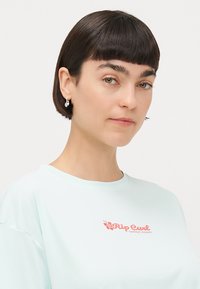 Ljust blå t-shirt med kort ärm med rundad halsringning och en korallfärgad logotyp "Rip Curl Surfing Company" på bröstet. Slät textur.