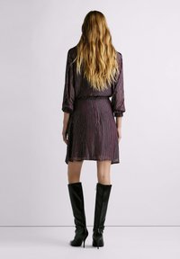 Vestito a righe viola con maniche lunghe, vita aderente e orlo corto, abbinato a eleganti stivali neri al ginocchio. Tessuto e finitura strutturati.