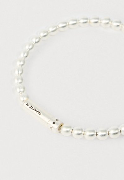 Brățară din mărgele argintii cu un închizător cilindric gravat "le gramme" pe un fundal deschis.