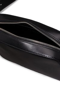 Czarna skórzana torba o gładkiej fakturze, srebrny metalowy zamek błyskawiczny oraz widoczne szwy wzdłuż krawędzi. Wnętrze ma ciemne wykończenie.