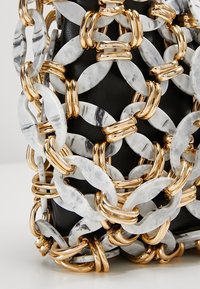 Czarna skórzana powierzchnia pokryta powiązanymi dużymi marmurowymi białymi i złotymi metalowymi owalnymi łańcuchami.