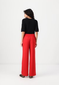 Haut noir à manches courtes associé à un pantalon large rouge avec une taille élastique. Des chaussures à imprimé animal complètent la tenue.