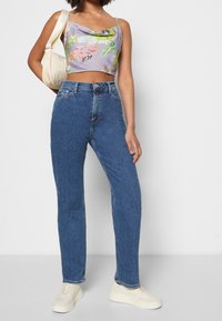 Top corto de flores en color lavanda con tirantes finos, combinado con jeans de pierna recta de talle alto en azul y zapatillas de color claro.