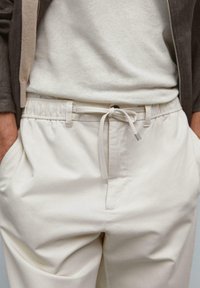 Light beige pants with an elastic waistband and drawstring. Smooth cotton fabric with side pockets and minimal stitching details.