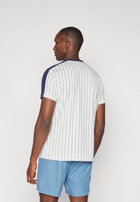 Kortermet skjorte i hvit med marineblå detaljer og vertikale striper. Laget av bomullsblanding, avslappet passform, rund hals. Kombinert med lyseblå shorts.