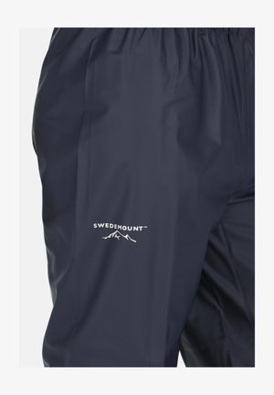 Granatowe wodoodporne spodnie z elastycznym pasem, z białym logo "SWEDEMOUNT" oraz graficznym motywem góry z lewej strony. Gładka tekstura.
