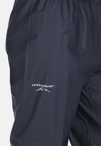 Marineblaue wasserdichte Hose mit elastischem Bund und einem weißen Logo "SWEDEMOUNT" mit Berggrafik auf dem Oberschenkel gedruckt.