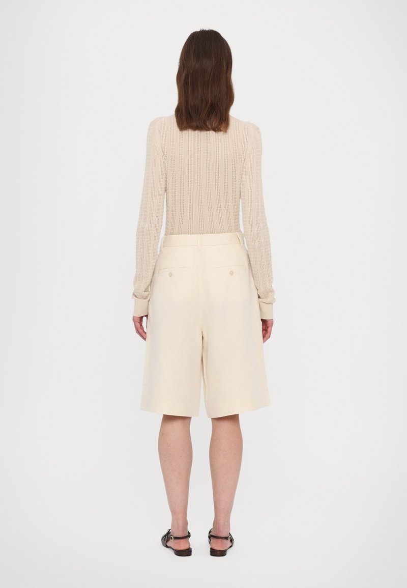 Beżowy sweter dziany z długimi rękawami i prążkowaną fakturą, w połączeniu z jasnymi kremowymi szortami z dwoma tylnymi kieszeniami i dopasowanym krojem.