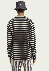 Langärmliges Shirt mit marineblauen und cremefarbenen Streifen, aus Baumwollmaterial, Rundhalsausschnitt und gerippten Bündchen; kombiniert mit gestreiften Hosen und einem marineblauen Bucket Hat.