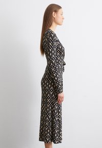 Robe midi à manches longues en noir et beige, ornée d'un motif géométrique. Le tissu est lisse avec une taille cintrée et une jupe évasée.