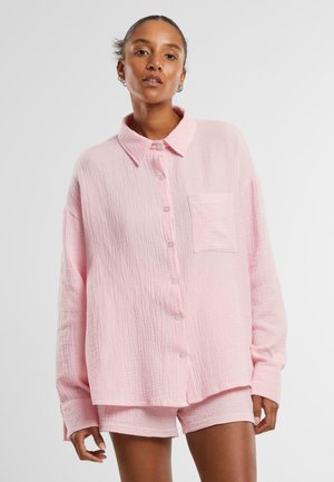 Pink, textured button-up shirt with a collar and single chest pocket, paired with matching shorts; both feature a relaxed fit.