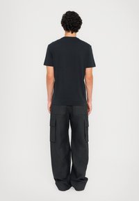 T-shirt preta de gola redonda combinada com calças cargo largas pretas com vários bolsos, apresentando um design casual e funcional.