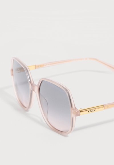 Lunettes de soleil carrées avec montures translucides roses, verres dégradés gris et branches dorées gravées du logo "Chloé".