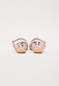 Rosa metalliska sandaler med öppen bakkant, justerbara hälremmar och platta sulor. Slät yta med en glänsande finish och minimalistisk design.
