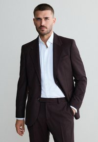 Dunkelburgunderfarbener Anzug mit strukturiertem Finish, ausgestattet mit einem Revers, zwei Knöpfen und einem weißen Hemd darunter, minimalistischem Design.