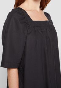Robe en coton noir avec un décolleté carré, des manches courtes bouffantes et des détails froncés le long des épaules pour plus de texture.