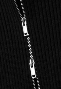 Tissu côtelé noir avec une fermeture éclair argentée partiellement ouverte, comprenant de multiples dents et un curseur pour une utilisation facile. La texture semble douce et texturée.