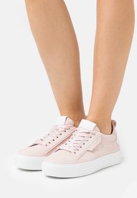 Jasnoróżowe trampki o gładkiej teksturze, białe sznurówki i biały język, z grubą białą gumową podeszwą oraz subtelnymi bocznymi akcentami.