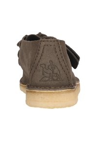 Brun mockaskor med en beige sula, som har en sydd design och en dekorativ präglad kamellogo på hälen.