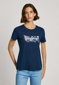 T-shirt en coton bleu marine à manches courtes. Présente un motif graphique floral en blanc, orange et bleu avec le texte "Pepe Jeans London" au centre.
