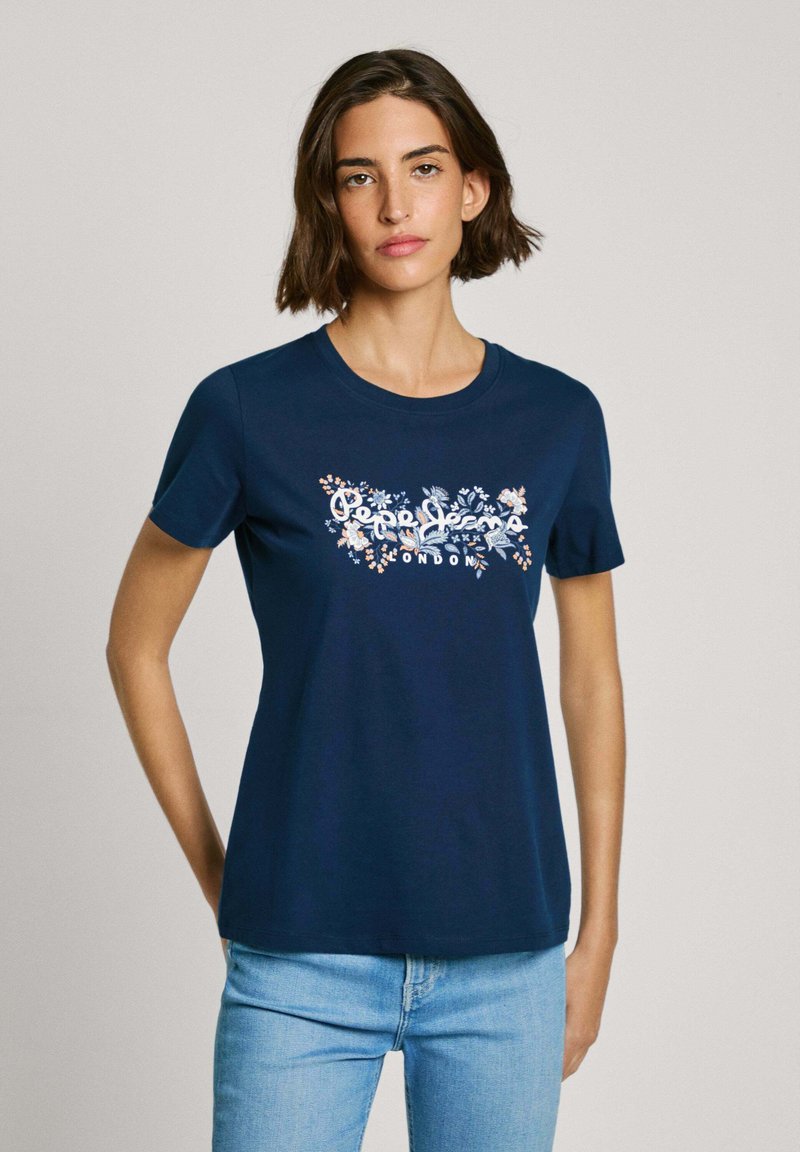 T-shirt en coton bleu marine à manches courtes. Présente un motif graphique floral en blanc, orange et bleu avec le texte "Pepe Jeans London" au centre.