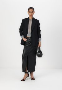 Blazer nero su misura sopra un maglione grigio a fantasia, abbinato a una gonna di pelle nera con spacco frontale e tacchi neri con cinturino.