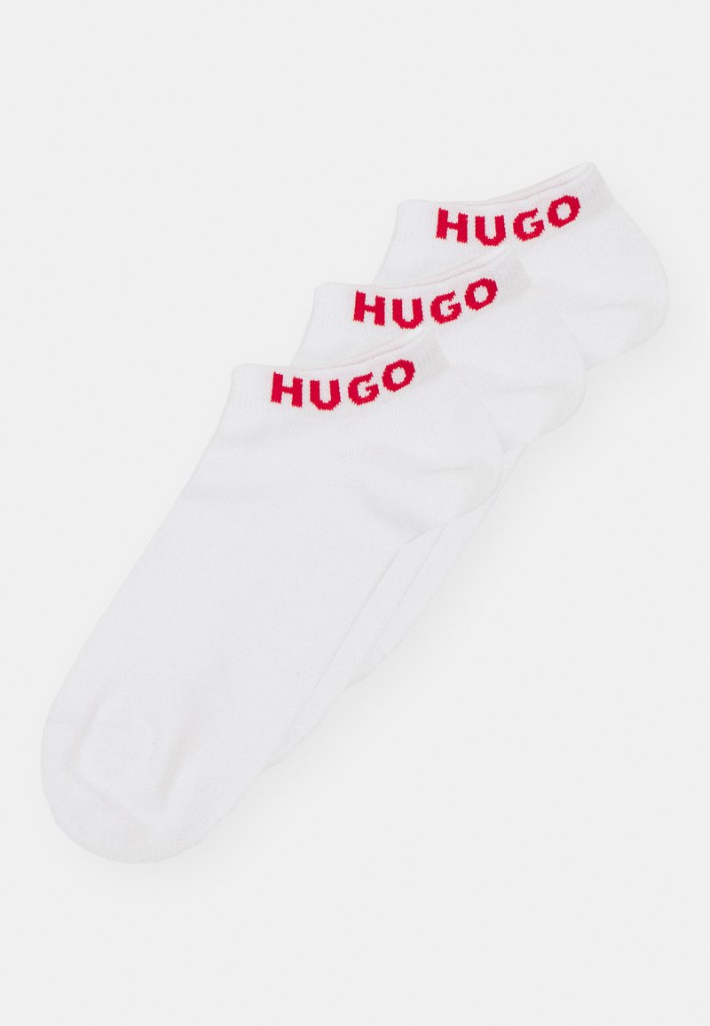 Három pár alacsonyvágású, fehér zokni, melyek piros "HUGO" logóval díszített mandzsettájukkal, sima textúrával és standard sportos fazonnal rendelkeznek.