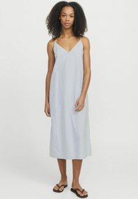 Vestido midi de rayas azul claro con tirantes finos, escote en V, tejido fluido y una silueta relajada. Llevado con chanclas marrones.