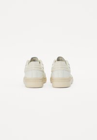 Skórzane sneakersy w odcieniu off-white z teksturowaną, brązową gumową podeszwą. Posiadają smukły design i minimalistyczne akcenty z tyłu.