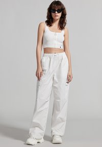 Top corto bianco con zip abbinato a pantaloni cargo bianchi con tasche laterali, completato da sneaker bianche chunky.