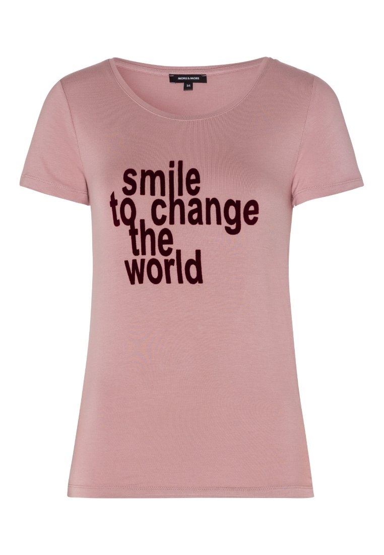 Camiseta de manga corta de color rosa claro con escote redondo que presenta un texto en negrita negro: "sonríe para cambiar el mundo". Tela suave con una textura lisa.