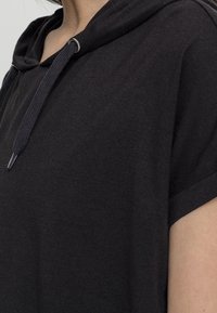 Svart hoodie med mjuk textur, korta ärmar och huva med dragsko. Har en minimalistisk design och sidovisibilitet.