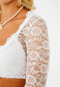Weißes Spitzenoberteil mit floralen Mustern, langen durchsichtigen Ärmeln und einem gewellten Ausschnitt. Weiches Material mit einer figurschmeichelnden Passform.