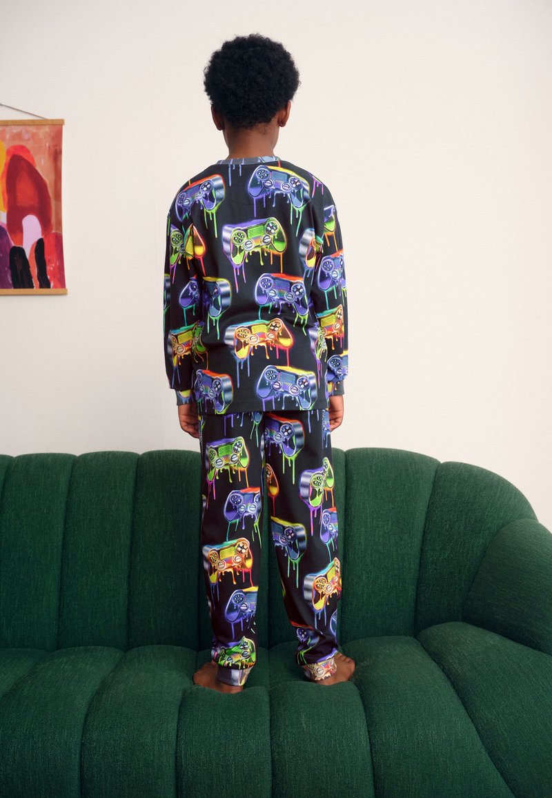 Farverigt pyjamasæt med langærmet top og bukser, lavet af blødt stof med print af en spilcontroller og et farverigt drypdessin på en mørk baggrund.
