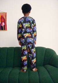 Set de pijamale colorat, alcătuit din bluză cu mâneci lungi și pantaloni, confecționat dintr-un material moale, cu imprimeu de controler de joc și design picurat colorat pe un fundal închis la culoare.