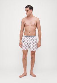 Beli boxer kratke hlače z ponovljenim vzorcem majhnega rdečega in črnega besedila ter ikon. Elastični pas z znamko 'Almaour'.