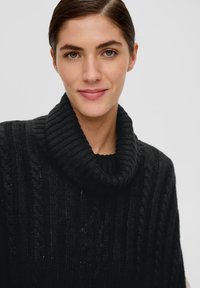 Zwarte kabelgebreide trui met een brede geribbelde col en gestructureerde patronen. Warm materiaal ontworpen voor comfort en lagen.