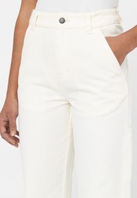 Kritvita bomullsbyxor med rak skärning, utrustade med knappstängning framtill, sidofickor och synliga sömdetaljer.