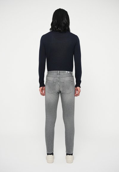 Ανδρικό μπλε φούτερ με εφαρμογή και γκρι τζιν, που αναδεικνύει κομψό σχέδιο, απαλή υφή και διακριτική φθορά, συνδυασμένο με αθλητικά παπούτσια σε ανοιχτό χρώμα.