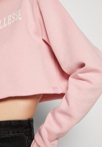 Felpa corta rosa realizzata in un materiale morbido, con un logo bianco sul petto e una piccola etichetta del marchio sull'orlo. Maniche texturizzate.