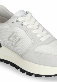 Sneaker bianca con una tomaia in rete testurizzata e accenti in suede, dotata di lacci bianchi, un logo prominente e una suola spessa in gomma nera.