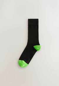 Čierna ponožka s nízkym lemom s jasne zelenými časťami na špičke a päte na svetlom pozadí.