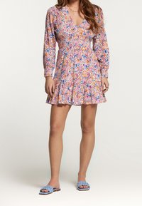 Vestido floral de manga corta con escote en V, cintura fruncida y falda en capas. Los colores incluyen rosa, azul, naranja y blanco. Combinado con sandalias deslizantes azules.