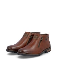 Paire de bottines en cuir marron avec fermetures éclair latérales et semelles en caoutchouc noir présentées sur fond blanc.