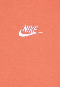 Nike majica v koralni barvi, izdelana iz mehkega bombaža, z belim vezenim logotipom in klasičnim ovratnikom.